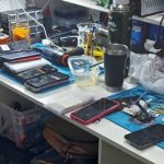 Bancada de trabalho com celulares, ferramentas e equipamentos eletrônicos.