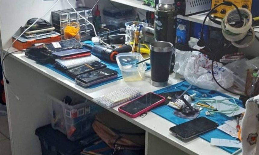 Bancada de trabalho com celulares, ferramentas e equipamentos eletrônicos.