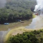 Barcos em chamas em rio na Amazônia, com fumaça negra e branca.