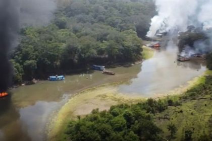 Barcos em chamas em rio na Amazônia, com fumaça negra e branca.