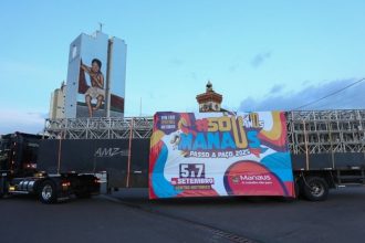 Caminhão com banner '#Sou Manaus Passo a Paço 2025' em frente a prédio com grafite.