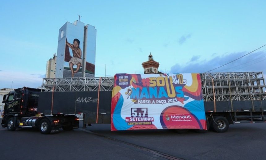 Caminhão com banner '#Sou Manaus Passo a Paço 2025' em frente a prédio com grafite.