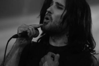 Cantor com cabelo longo cantando no microfone