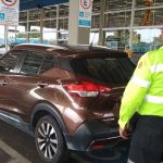 Carro marrom em vaga especial levando multa para deficientes com guarda de trânsito ao lado.