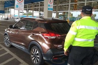 Carro marrom em vaga especial levando multa para deficientes com guarda de trânsito ao lado.