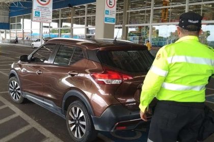 Carro marrom em vaga especial levando multa para deficientes com guarda de trânsito ao lado.