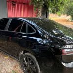 Carro preto que foi abordado na avenidas das Torres estacionado em frente a um galpão vermelho e vegetação