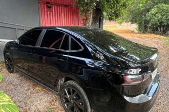 Carro preto que foi abordado na avenidas das Torres estacionado em frente a um galpão vermelho e vegetação