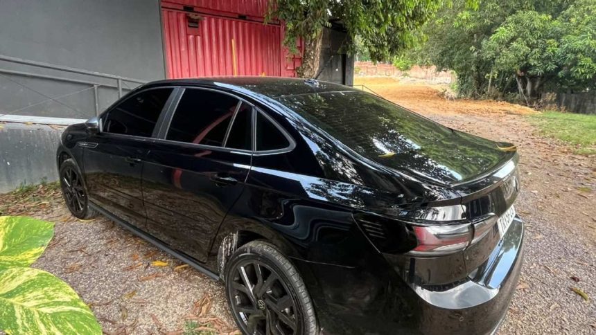 Carro preto que foi abordado na avenidas das Torres estacionado em frente a um galpão vermelho e vegetação