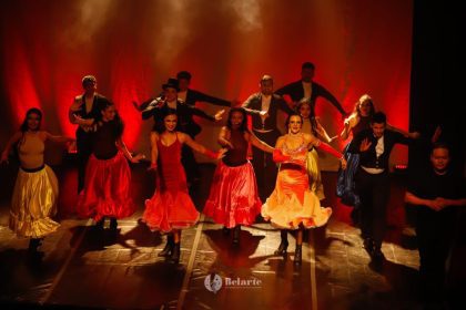 Cena de dança vibrante no palco do Teatro Amazonas, com figurinos coloridos e luzes dramáticas.