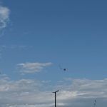 Céu azul de calor com nuvens e pipas voando, criando um cenário de dia ensolarado.