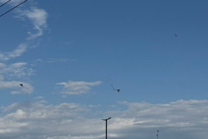 Céu azul de calor com nuvens e pipas voando, criando um cenário de dia ensolarado.