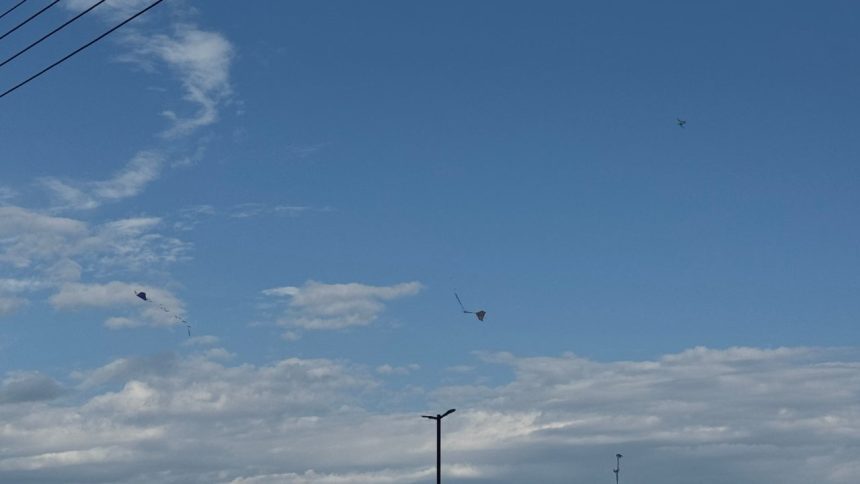 Céu azul de calor com nuvens e pipas voando, criando um cenário de dia ensolarado.