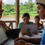 Comunidade indígena em reunião, utilizando laptops e acessando informações
