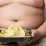 Criança obesa segurando um prato com batatas fritas.