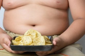 Criança obesa segurando um prato com batatas fritas.