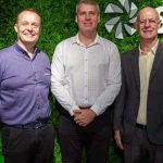 Diretores da Sicredi posam sorrindo em frente a logo da empresa.