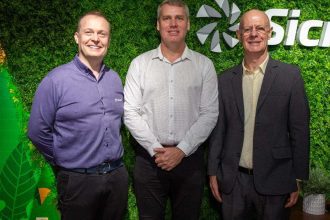 Diretores da Sicredi posam sorrindo em frente a logo da empresa.