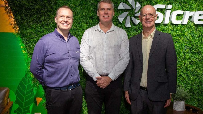 Diretores da Sicredi posam sorrindo em frente a logo da empresa.