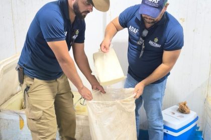 Dois homens em Parintis transferindo um bloco de produto embalado para um saco grande dentro de uma sala.