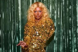 Drag queen com cabelo loiro encaracolado e vestido dourado brilhante.