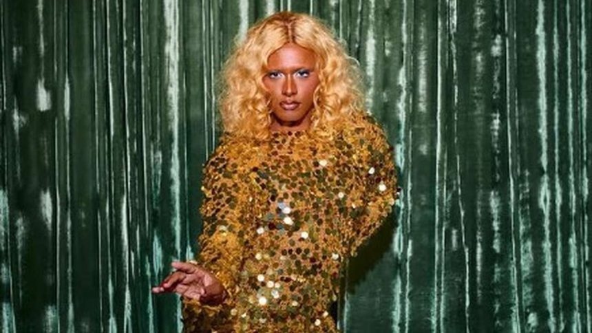 Drag queen com cabelo loiro encaracolado e vestido dourado brilhante.