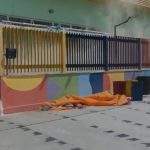 Princípio de incêndio na CMEI) Maria Emília Mestrinho, Duas mulheres perto de um prédio com fumaça, lixeiras e um pano laranja no chão.