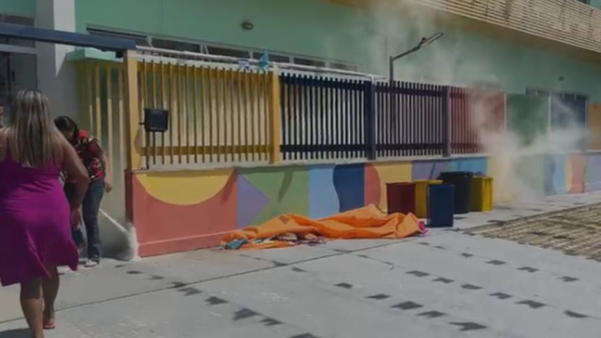 Princípio de incêndio na CMEI) Maria Emília Mestrinho, Duas mulheres perto de um prédio com fumaça, lixeiras e um pano laranja no chão.