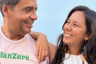Duas pessoas sorrindo, com um homem usando uma camiseta com a palavra 'Banzerê'.