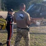 Equipe de resgate socorrendo paciente com ferimento no tornozelo, perto de helicóptero.
