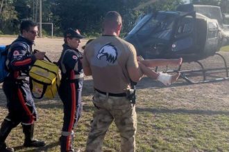 Equipe de resgate socorrendo paciente com ferimento no tornozelo, perto de helicóptero.