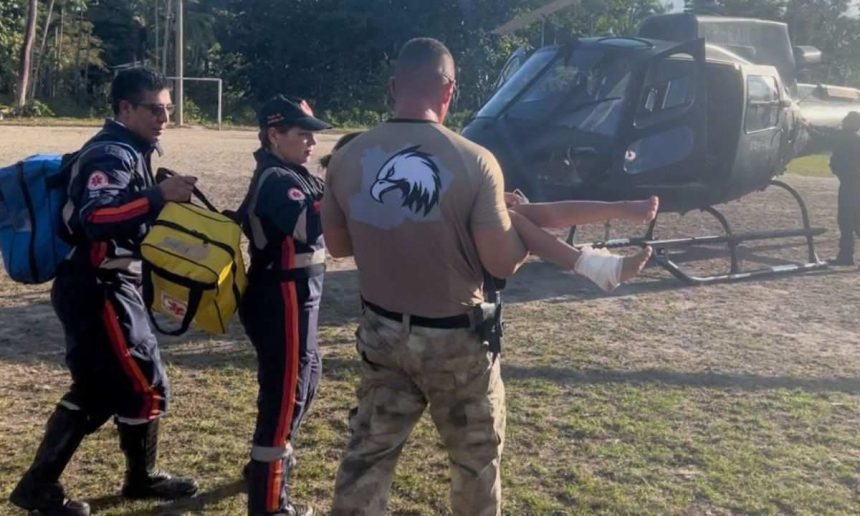 Equipe de resgate socorrendo paciente com ferimento no tornozelo, perto de helicóptero.