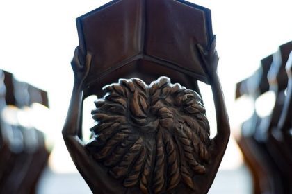 Estátuas segurando livros abertos do prêmio MEC, com foco em detalhes em bronze, simbolizando educação e conhecimento.