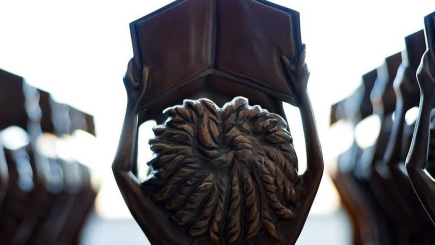 Estátuas segurando livros abertos do prêmio MEC, com foco em detalhes em bronze, simbolizando educação e conhecimento.