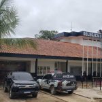 Fachada da delegacia de polícia de Eirunepé com viaturas e vegetação.