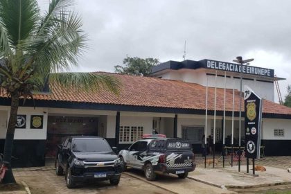 Fachada da delegacia de polícia de Eirunepé com viaturas e vegetação.