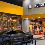Fachada da lanchonete JSK Burgers com fila de clientes e carro estacionado em frente.