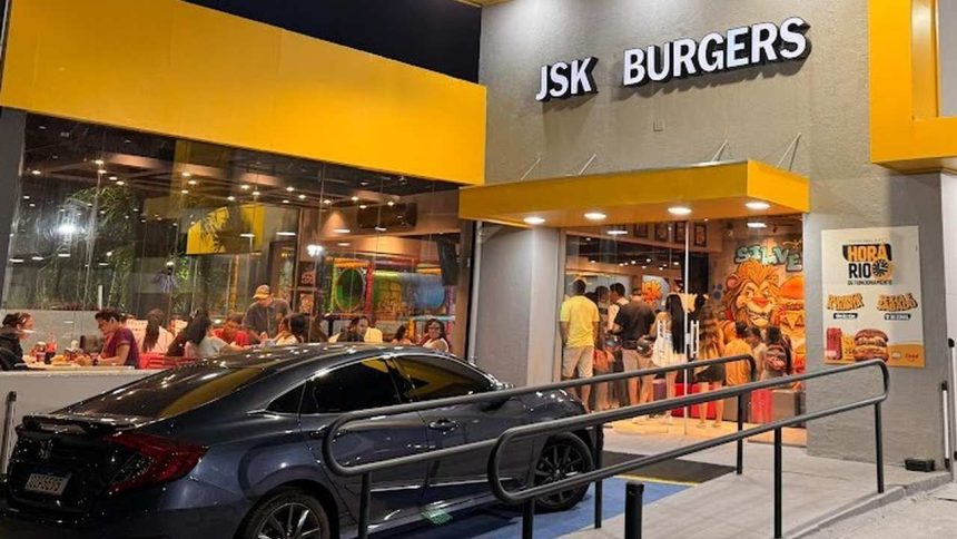Fachada da lanchonete JSK Burgers com fila de clientes e carro estacionado em frente.
