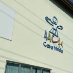 Fachada de prédio com logo 'AACV Casa Vida', em tons de azul, verde e marrom, e um desenho de uma pessoa.