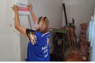 Fiscalização apreende alimentos irregulares em Manaus. Mulher coloca placa de interdição.