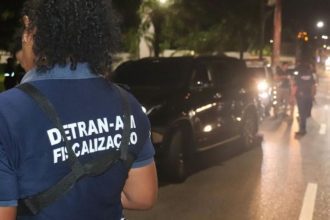 Fiscalização do Detran-AM em ação, com carro parado e agentes na rua.