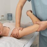 Fisioterapeuta realizando massagem no braço de paciente para aliviar dores.