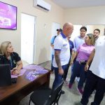 Wilson Lima, Funcionários e visitantes em um escritório, com destaque para uma tela com informações e pessoas interagindo.