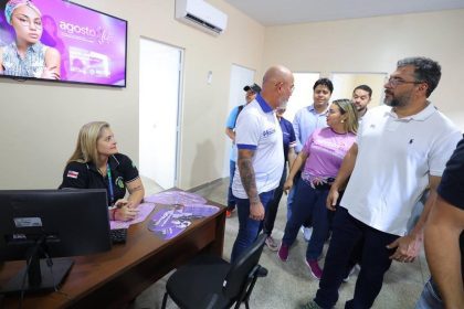 Wilson Lima, Funcionários e visitantes em um escritório, com destaque para uma tela com informações e pessoas interagindo.