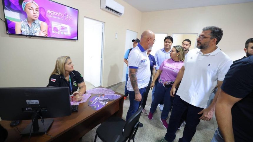 Wilson Lima, Funcionários e visitantes em um escritório, com destaque para uma tela com informações e pessoas interagindo.