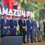 Grupo de homens em evento AMAZON ON, com banner e tema da Amazônia ao fundo.