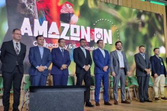 Grupo de homens em evento AMAZON ON, com banner e tema da Amazônia ao fundo.