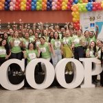 Grupo de pessoas com camisetas verdes posando em frente a letras grandes que formam a palavra COOP, em evento.