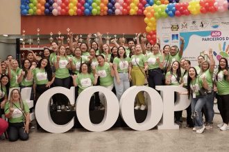 Grupo de pessoas com camisetas verdes posando em frente a letras grandes que formam a palavra COOP, em evento.