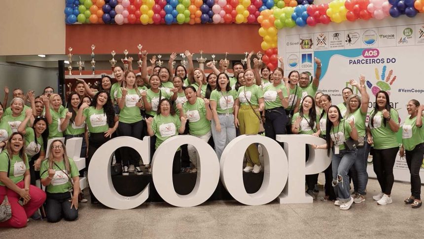 Grupo de pessoas com camisetas verdes posando em frente a letras grandes que formam a palavra COOP, em evento.